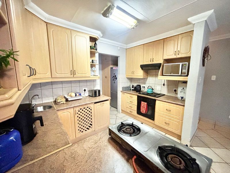 A functional kitchen featuring light wood-tone cabinetry, laminate countertops, built-in oven, hob, and extractor fan with tiled backsplash and flooring.