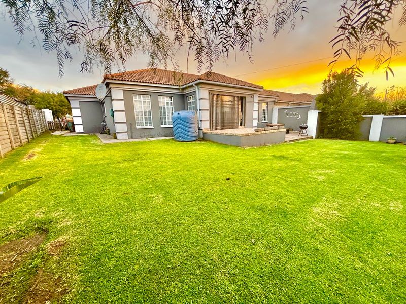 Rear view of the house featuring a spacious lawn, a paved patio area, and a water tank against a sunset backdrop.