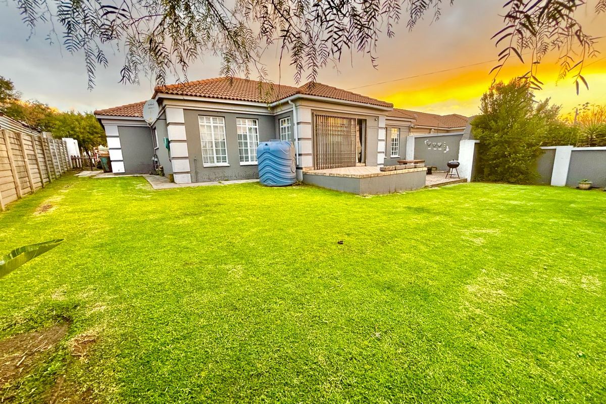 Rear view of the house featuring a spacious lawn, a paved patio area, and a water tank against a sunset backdrop.