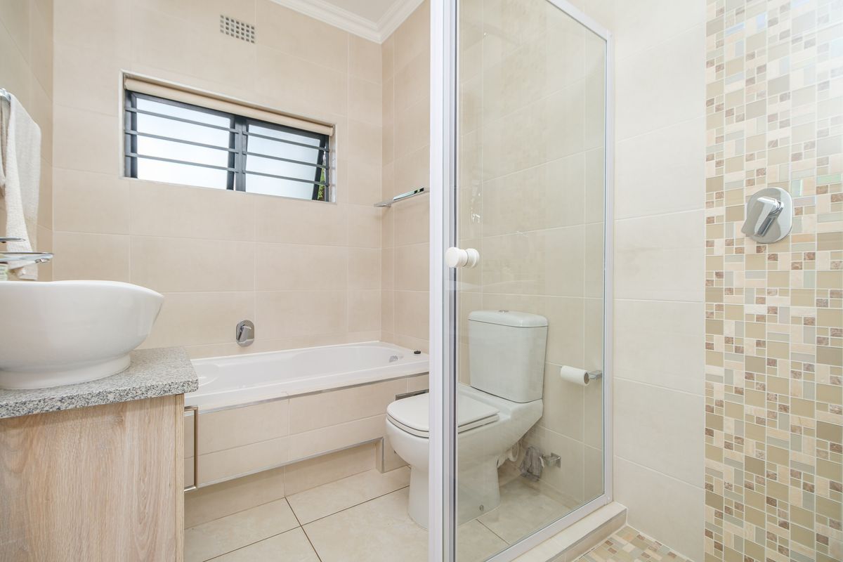 Modern bathroom featuring a built-in vanity with vessel sink, a bathtub, a separate shower enclosure, and neutral tiled finishes throughout.