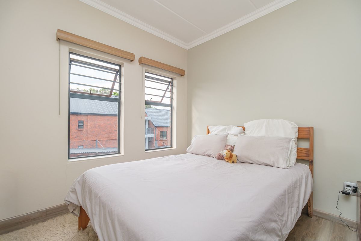 A well-maintained bedroom featuring neutral walls, laminate flooring, coved ceiling cornices, and dual louvered windows with timber pelmets.