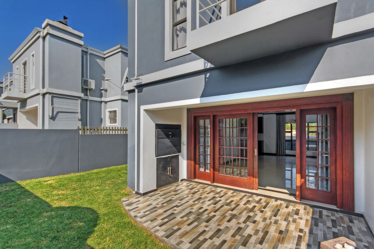 Rear exterior view of the townhouse featuring a paved patio with a built-in braai, sliding wooden doors, and a private lawn area.