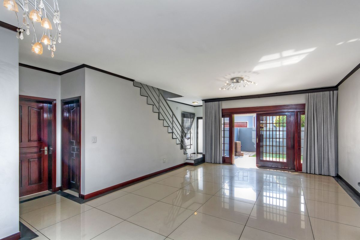 Spacious, light-filled living area featuring polished tile flooring, a modern staircase, and large wooden sliding doors opening to the exterior.