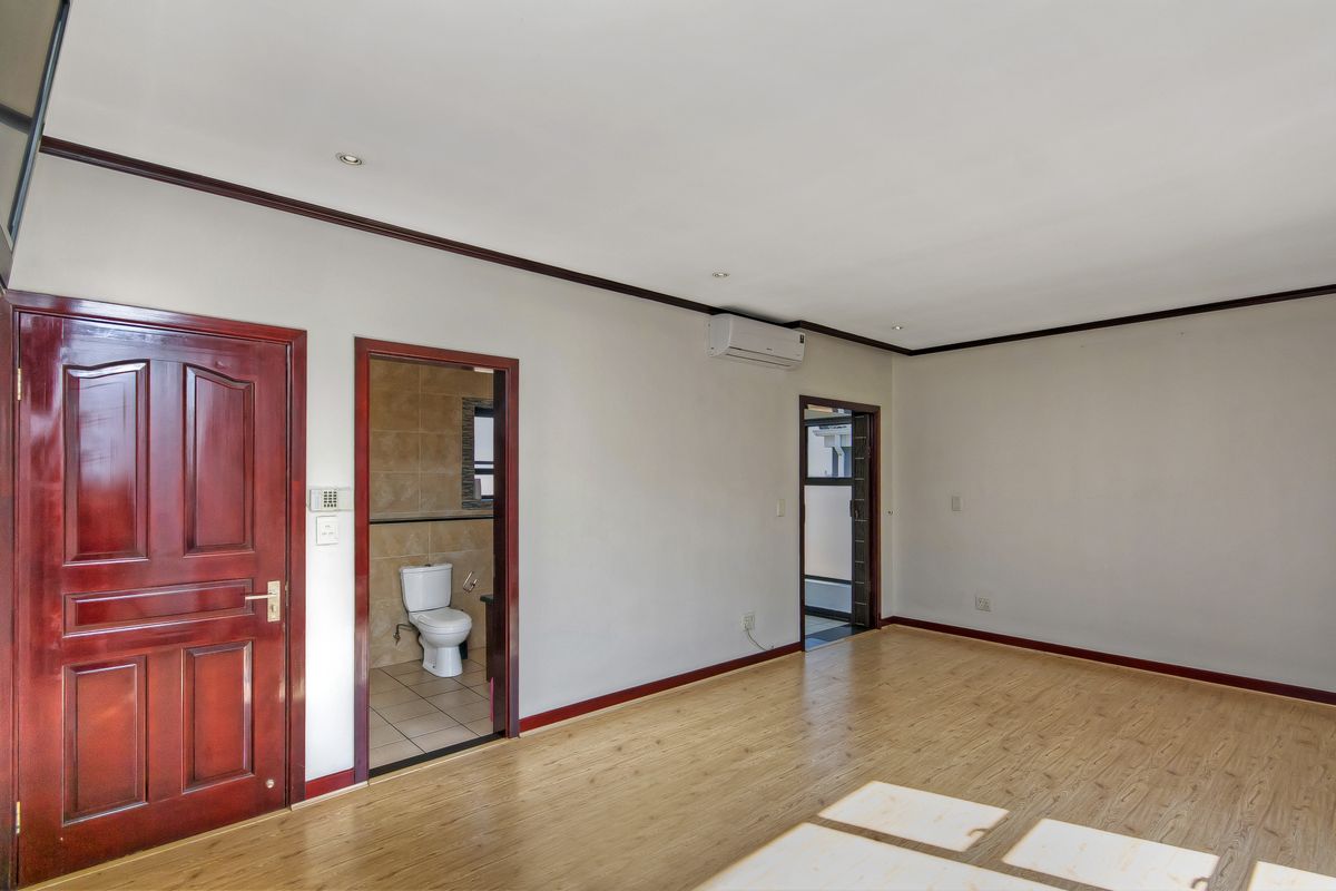 Spacious bedroom featuring laminate flooring, an air conditioning unit, and an en-suite bathroom with tiled finishes.