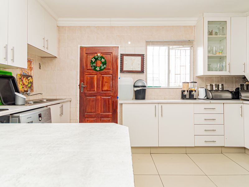 A functional kitchen featuring white cabinetry, tiled backsplash, laminate countertops, and tiled flooring, offering a practical layout with ample storage space.