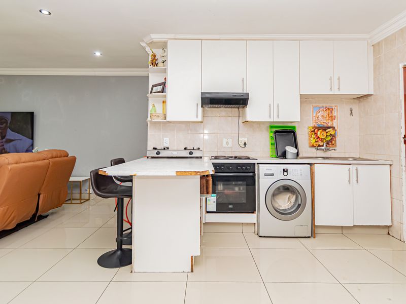 Open-plan kitchen and living area featuring white cabinetry, built-in oven, hob, and tiled flooring, offering a functional layout for modern living.