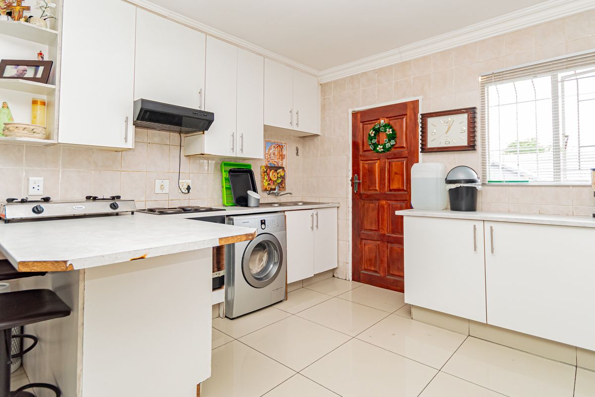 Functional kitchen featuring white cabinetry, tiled backsplash, integrated washing machine, and tiled flooring with direct access to the exterior.