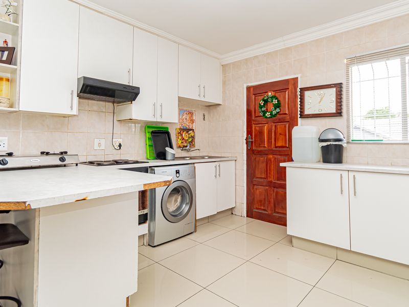 Functional kitchen featuring white cabinetry, tiled backsplash, integrated washing machine, and tiled flooring with direct access to the exterior.