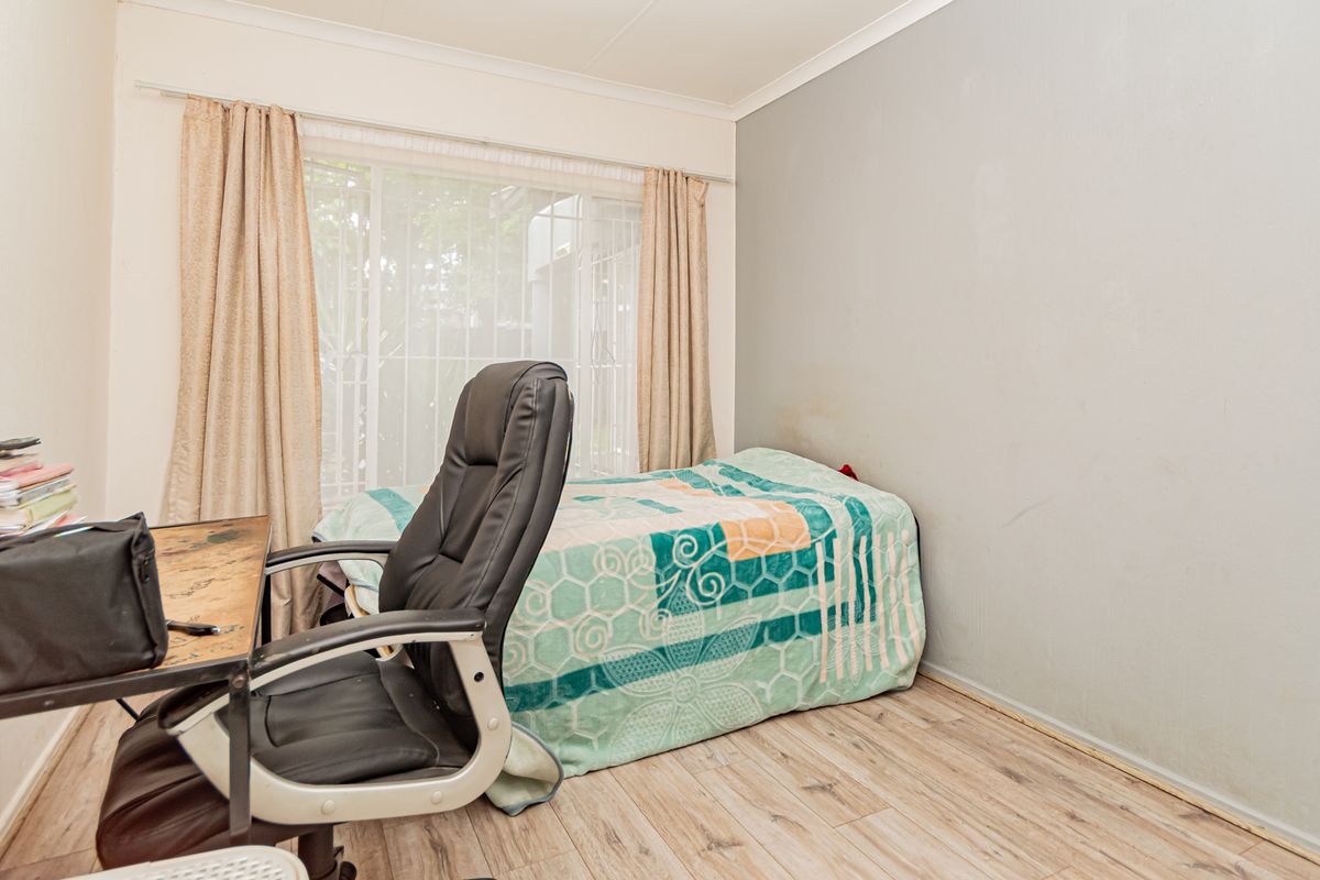 A functional bedroom featuring light-toned laminate flooring, neutral wall finishes, and large windows with curtain rails, offering a blank canvas for personalization.