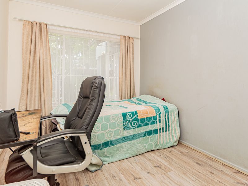A functional bedroom featuring light-toned laminate flooring, neutral wall finishes, and large windows with curtain rails, offering a blank canvas for personalization.