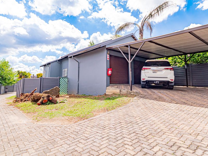 Front exterior view of the townhouse featuring a paved driveway, covered carport, and secure roller shutter garage door.