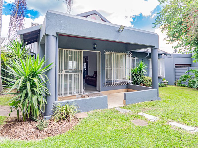 Rear view of the townhouse featuring a covered patio with tiled flooring, security bars on windows, and access to a private landscaped garden.
