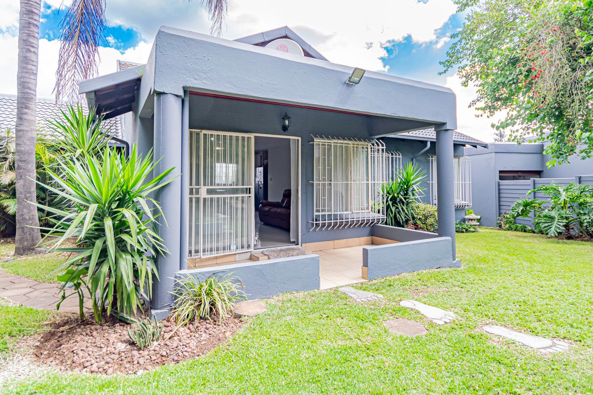 Rear view of the townhouse featuring a covered patio with tiled flooring, security bars on windows, and access to a private landscaped garden.