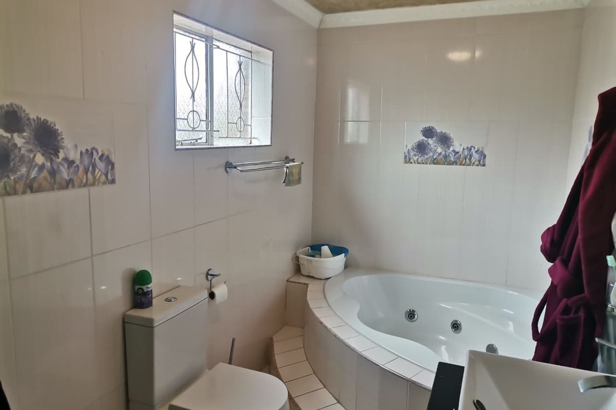 A functional bathroom featuring a built-in corner spa bath, ceramic wall tiles with decorative accents, and a standard toilet.