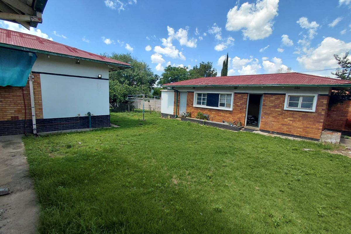 A view of the rear garden area featuring brick exterior walls, metal roofing, and a grass lawn between two building structures.