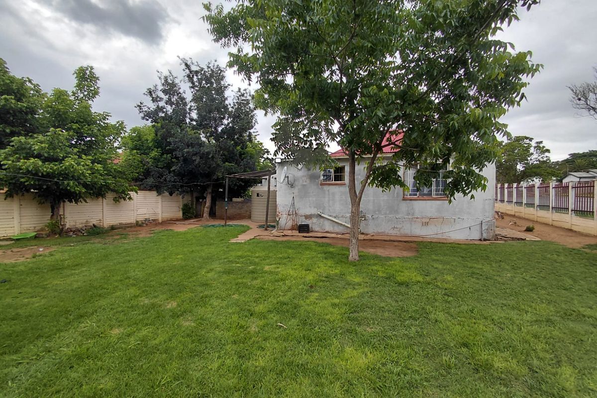 Rear view of the property featuring a spacious lawn, mature trees, perimeter wall fencing, and a water storage tank.