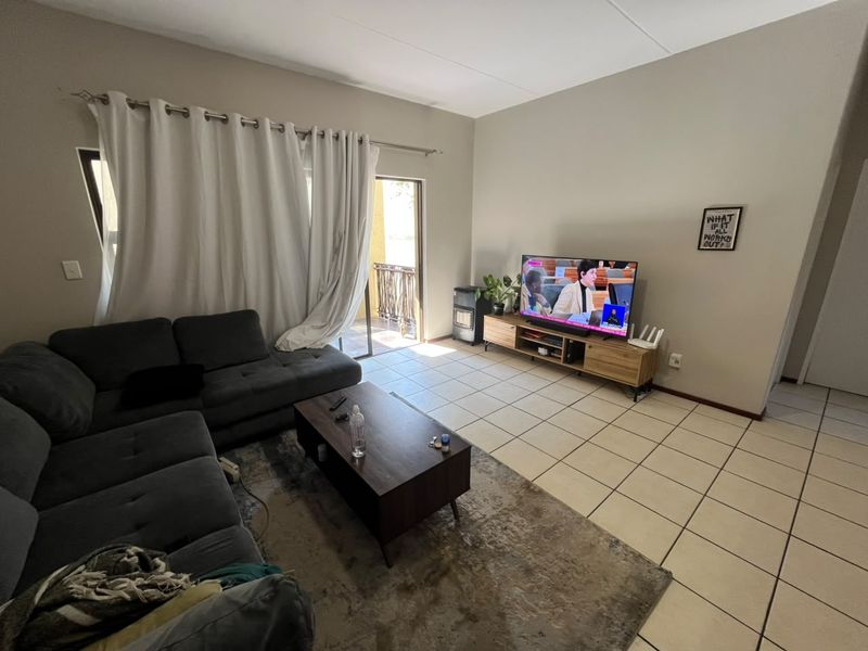 A spacious living room featuring neutral walls, tiled flooring, and a sliding glass door providing access to an outdoor balcony area.