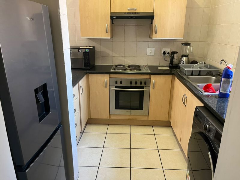 Compact kitchen featuring light wood cabinetry, granite countertops, built-in oven, electric hob, extractor fan, and tiled flooring.