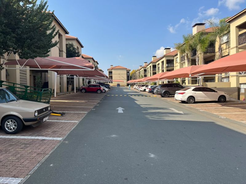 A view of the apartment complex driveway featuring multiple covered parking bays and multi-story residential buildings.