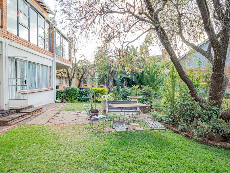 Rear view of the apartment building featuring a private garden, lawn, paved patio area, and mature trees.
