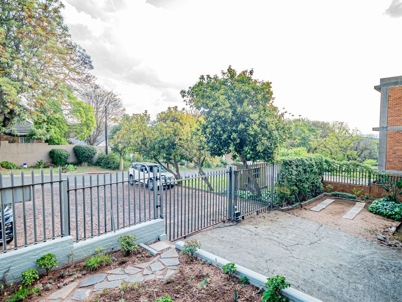 Exterior view of the apartment entrance featuring a paved driveway, metal security gate, and a tiled balcony area.