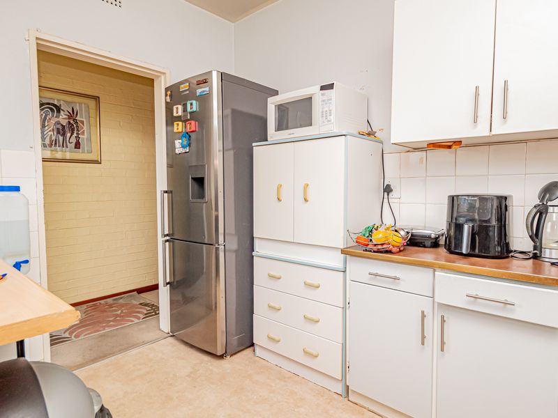 A functional kitchen featuring white cabinetry, laminate countertops, and a tiled backsplash, providing a practical layout with direct access to an adjacent hallway.