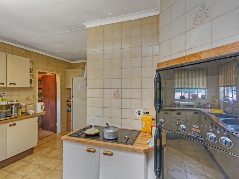A dated kitchen featuring original cabinetry, ceramic wall and floor tiles, and a built-in oven and hob, offering significant potential for modernization.