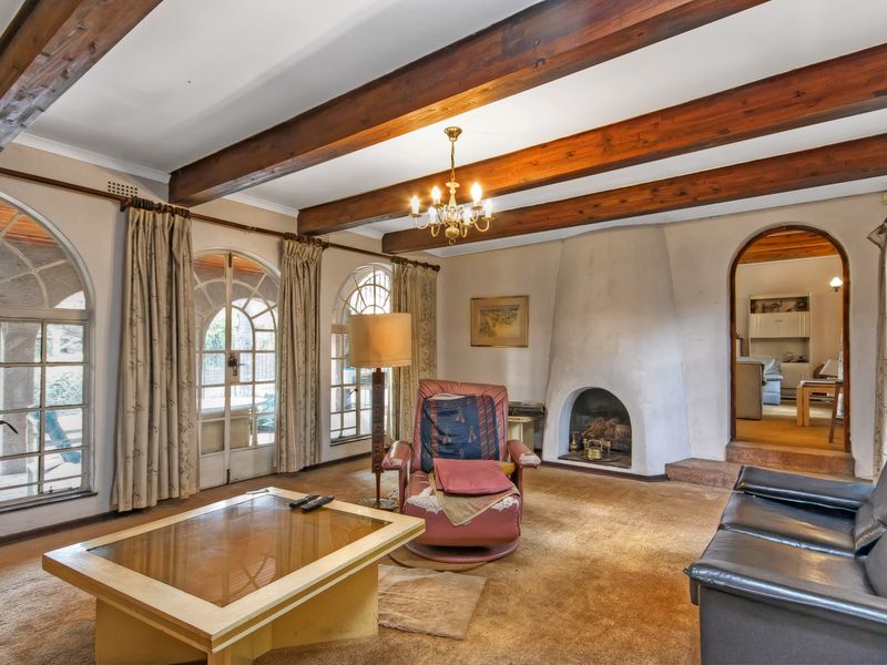 Spacious living room featuring exposed timber ceiling beams, an arched fireplace, and large arched windows providing natural light and garden access.