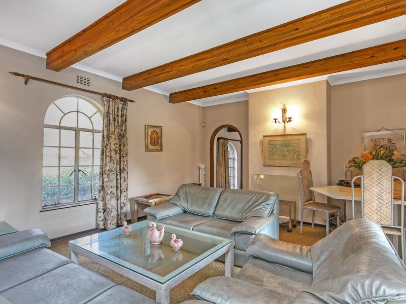 A cozy living room featuring exposed timber ceiling beams, an arched window, and an arched doorway, offering a classic and character-filled living space.