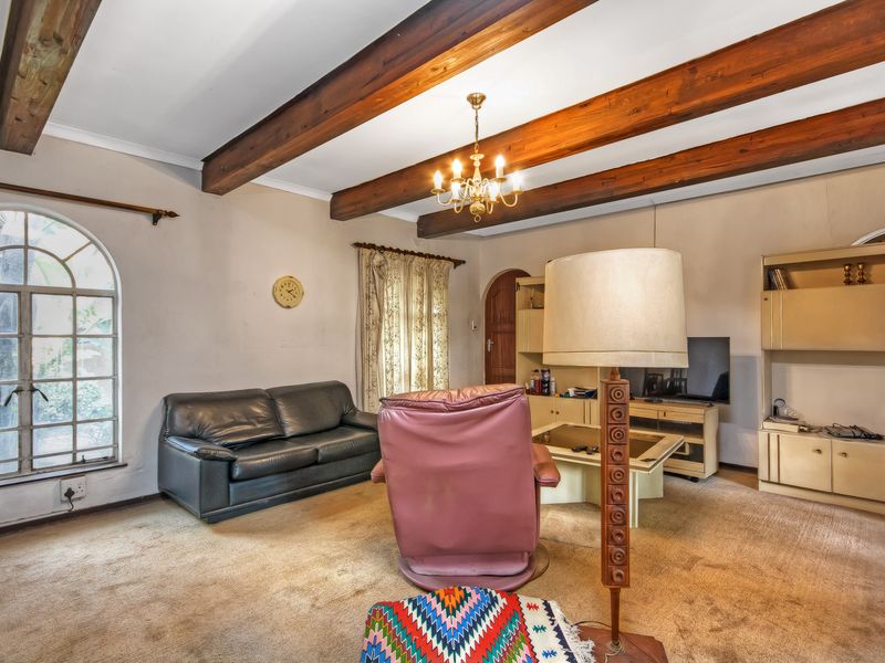 A living room featuring exposed timber ceiling beams, an arched window, and built-in cabinetry, offering a classic architectural foundation ready for modernization.