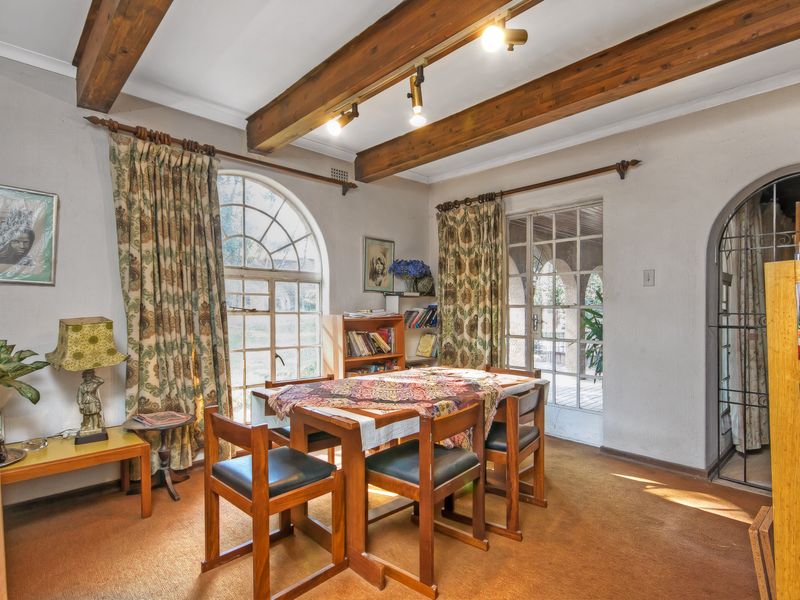 Dining room featuring exposed timber ceiling beams, an arched window, and an arched doorway leading to an outdoor area.