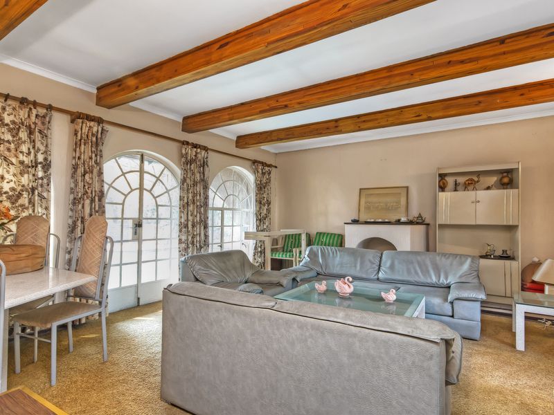Spacious living room featuring exposed timber ceiling beams, arched glass doors providing natural light, and a built-in fireplace mantle.