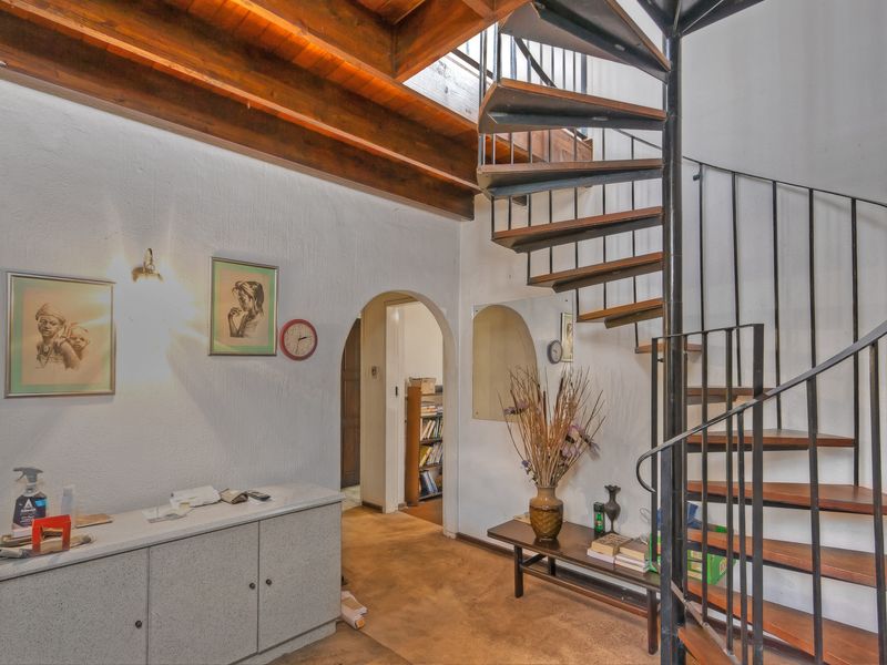 Entrance hallway featuring a prominent spiral staircase, exposed timber ceiling beams, and an arched doorway leading to adjacent living spaces.
