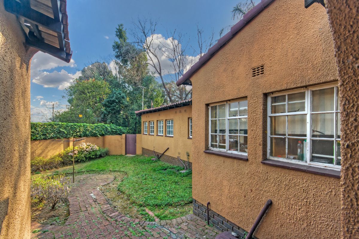 Rear exterior view of the property featuring a brick-paved pathway, established garden, and plastered building facade with steel-framed windows.
