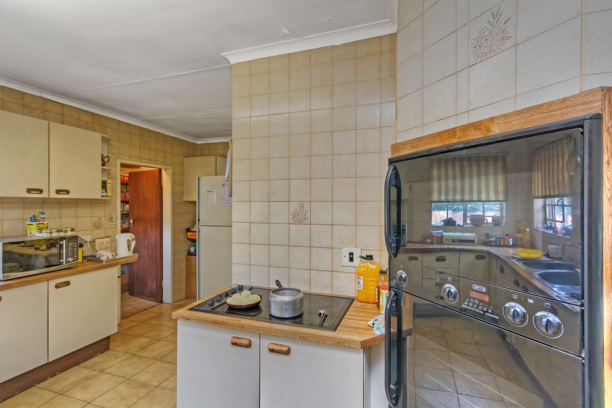 A dated kitchen featuring original cabinetry, ceramic wall and floor tiles, and a built-in oven and hob, offering significant potential for modernization.