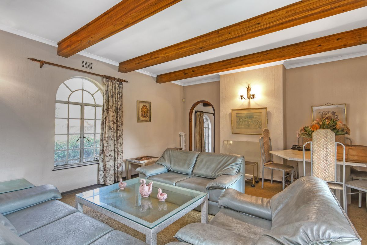 A cozy living room featuring exposed timber ceiling beams, an arched window, and an arched doorway, offering a classic and character-filled living space.
