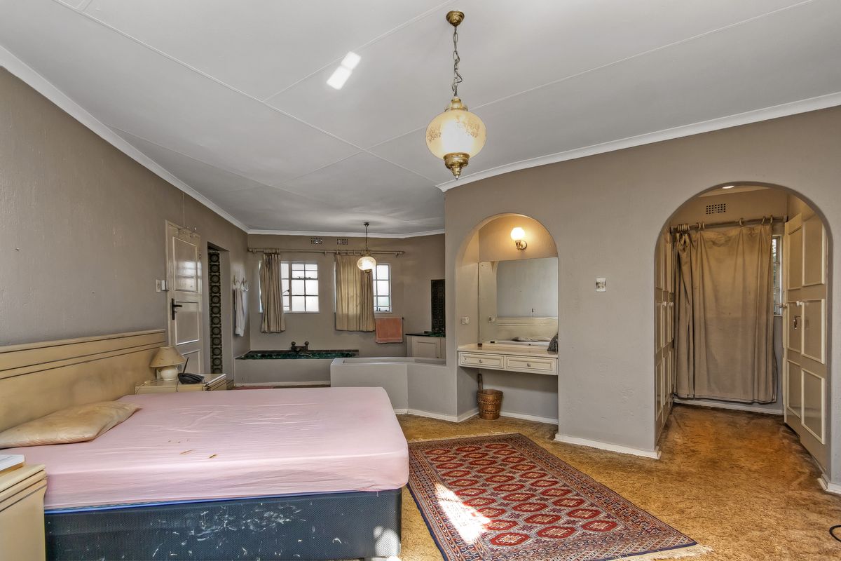 Spacious bedroom featuring an integrated vanity area, built-in cupboards, and an open-plan sunken bathtub, offering potential for a modern ensuite renovation.