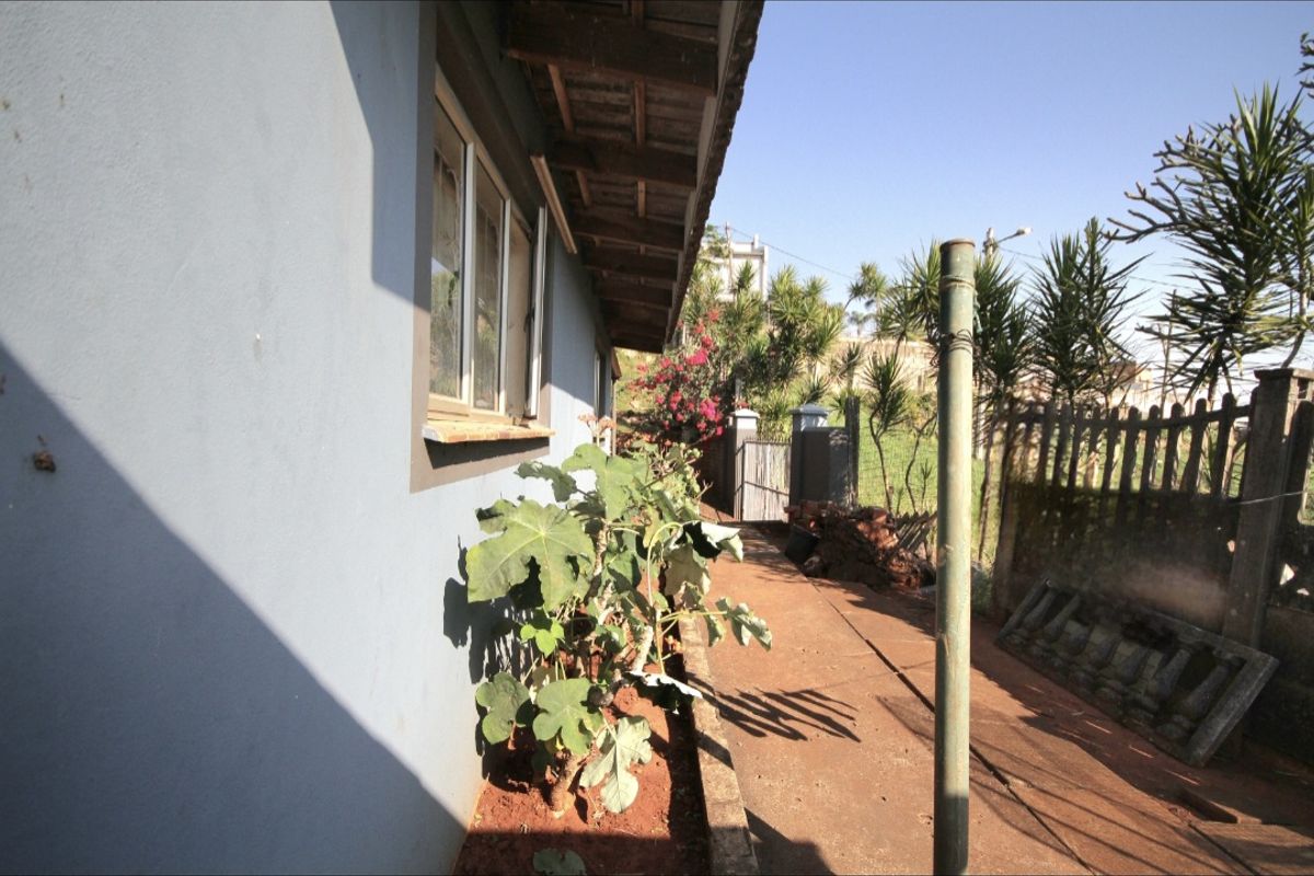 A side exterior view of the property showing a concrete pathway, boundary fencing, and the building's exterior wall and roof eaves.