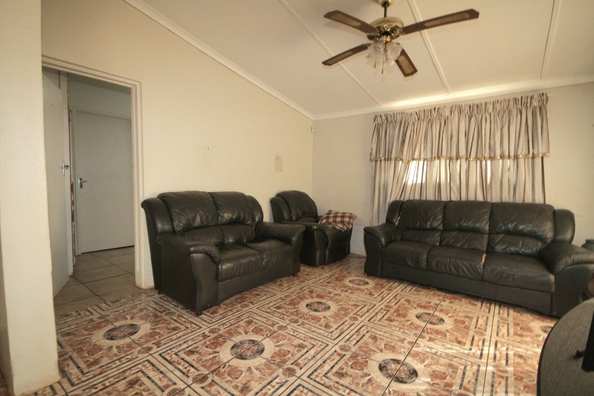 A living room featuring tiled flooring and a ceiling fan, offering a dated aesthetic that could be updated with modern finishes.