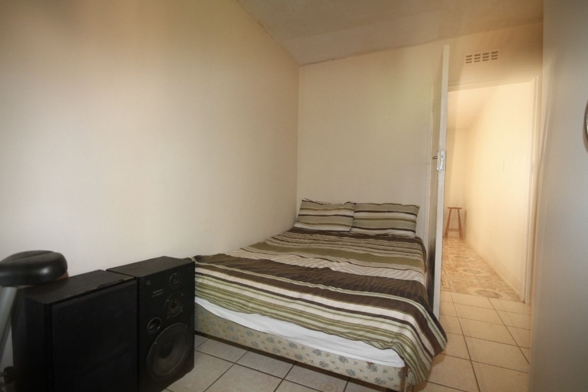 A compact bedroom featuring tiled flooring and neutral wall finishes, providing a functional sleeping space with direct access to an adjacent hallway.