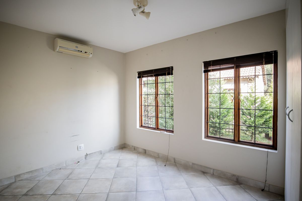 An empty bedroom featuring tiled flooring, wooden window frames with security bars, and a wall-mounted air conditioning unit.