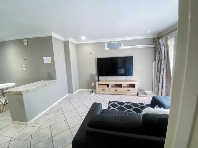 Living room featuring tiled flooring, crown molding, and a pass-through counter, showing signs of wear on the walls and requiring cosmetic updates.