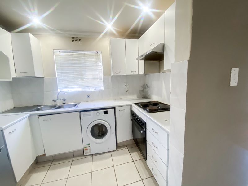 Functional kitchen featuring white cabinetry, built-in oven and hob, stainless steel sink, and tiled flooring with integrated laundry appliance space.
