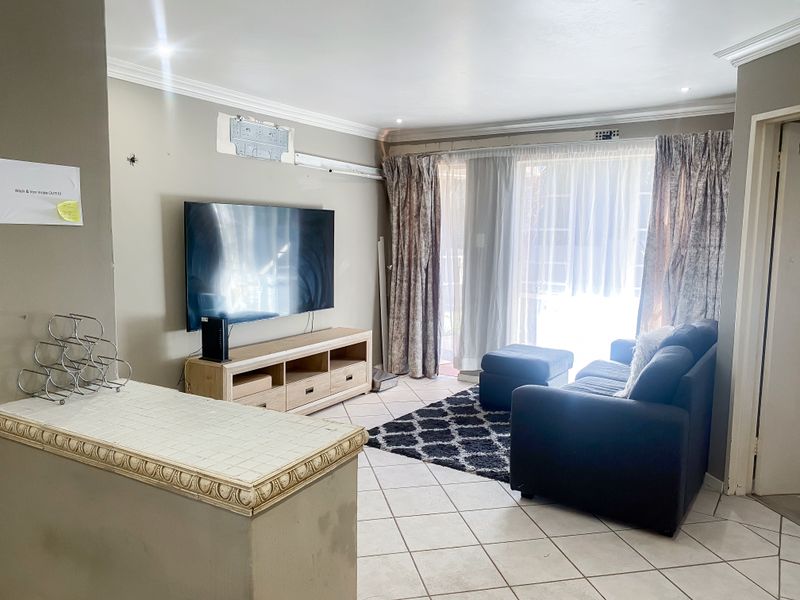 A living room featuring tiled flooring, crown molding, and a tiled breakfast bar, with direct access to an outdoor area through sliding glass doors.