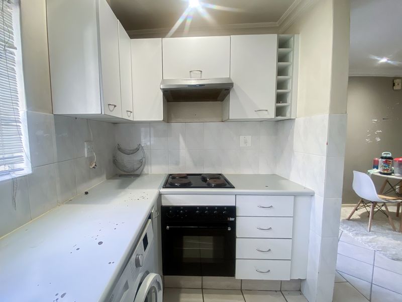 Compact kitchen featuring white cabinetry, built-in oven and hob, extractor fan, and tiled splashbacks, offering a functional layout for daily meal preparation.