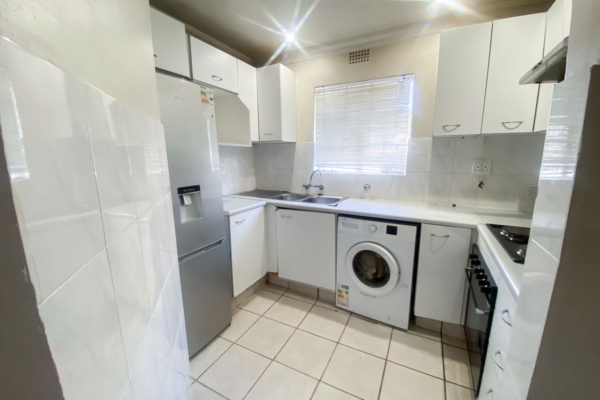 Compact kitchen featuring white cabinetry, tiled backsplash, tiled flooring, and integrated appliances including an oven, hob, and extractor fan.