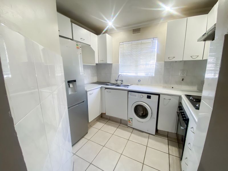 Compact kitchen featuring white cabinetry, tiled backsplash, tiled flooring, and integrated appliances including an oven, hob, and extractor fan.