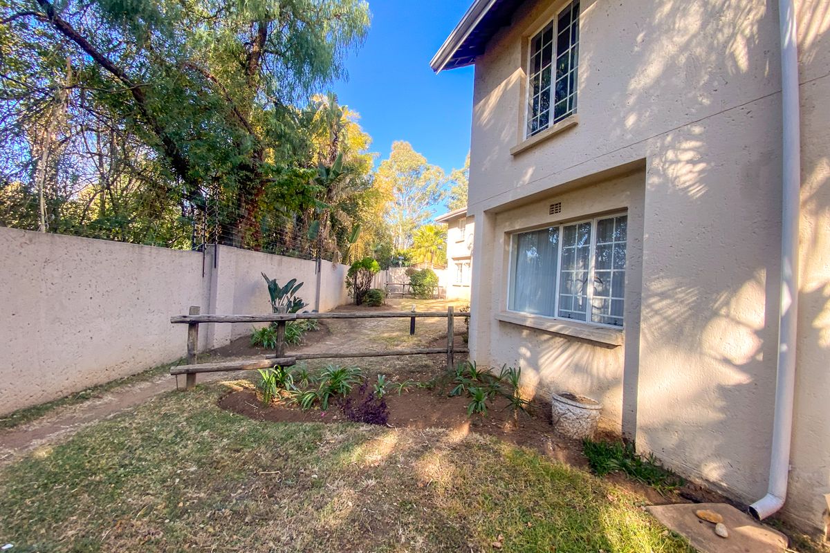 A rear exterior view of the apartment featuring a private garden area, plastered boundary walls with electric fencing, and established garden beds.