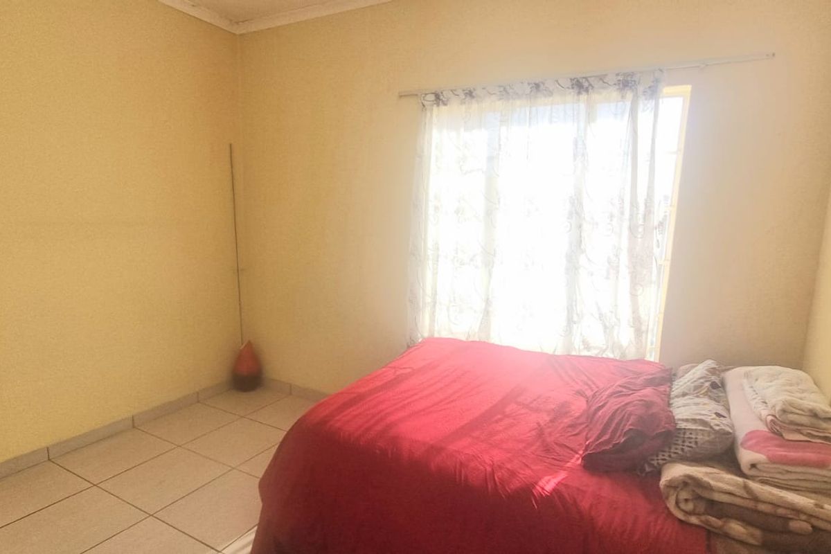 A simple bedroom featuring tiled flooring and a window with curtain rail, providing a functional and neutral space.