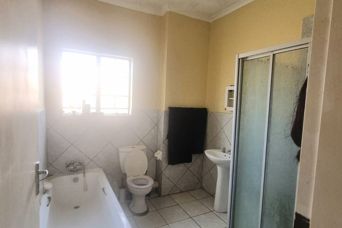 A functional bathroom featuring a bathtub, pedestal basin, and a separate shower enclosure with tiled flooring and walls.
